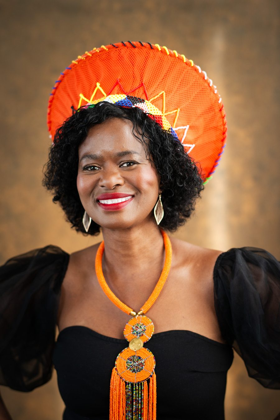 Tae Betty smiling — warm portrait with an orange headpiece